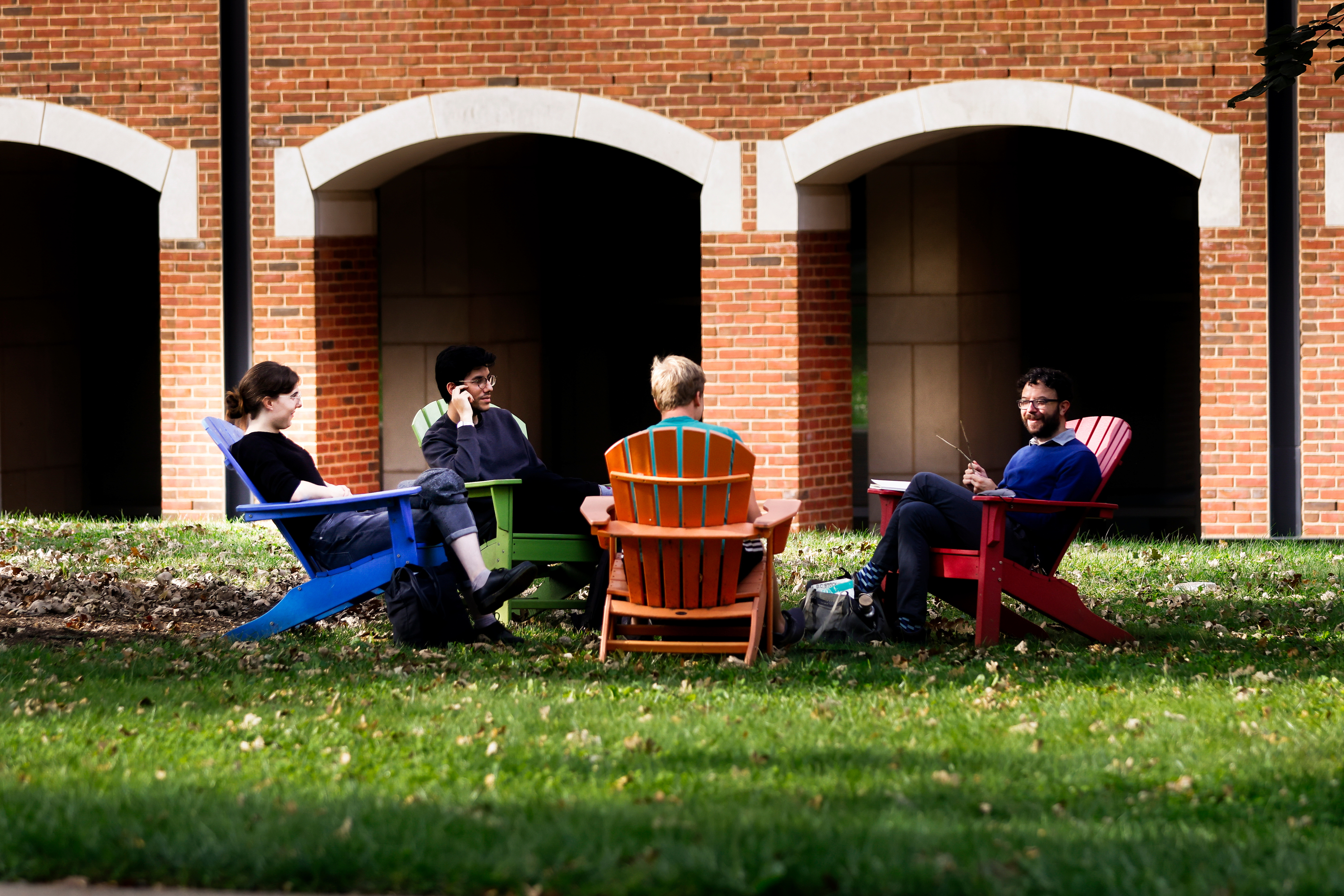 students sitting in lawn chairs conversing in front of academic building