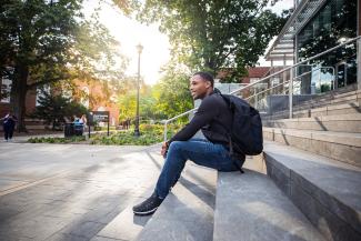 student on steps outside with sun and backpac
