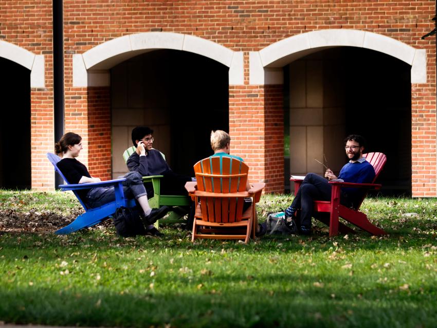 students sitting in lawn chairs conversing in front of academic building