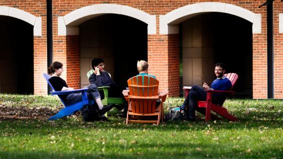 students sitting in lawn chairs conversing in front of academic building