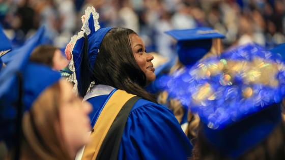grad student sitting in rupp arena during ceremony smiling looking up with masters regalia