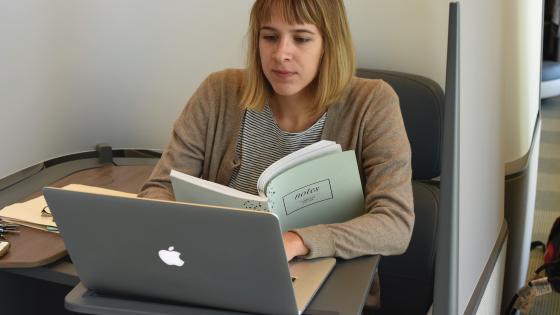student writing on laptop in library with book