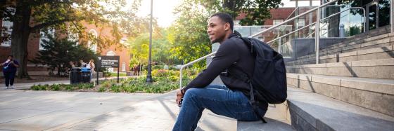 student on steps outside with sun and backpac